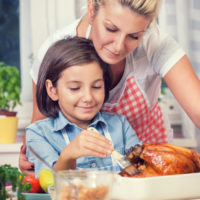 A child and mother basting a chicken.