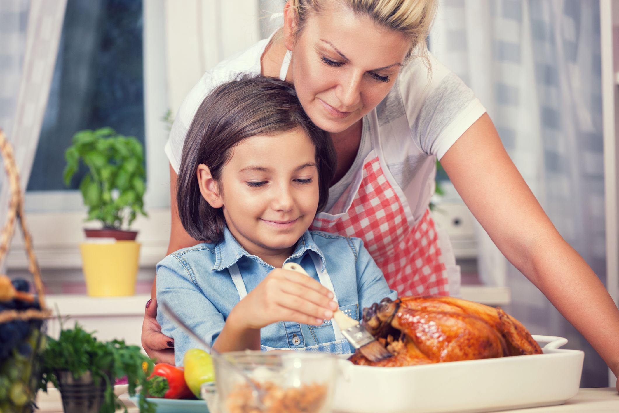 A child and mother basting a chicken.