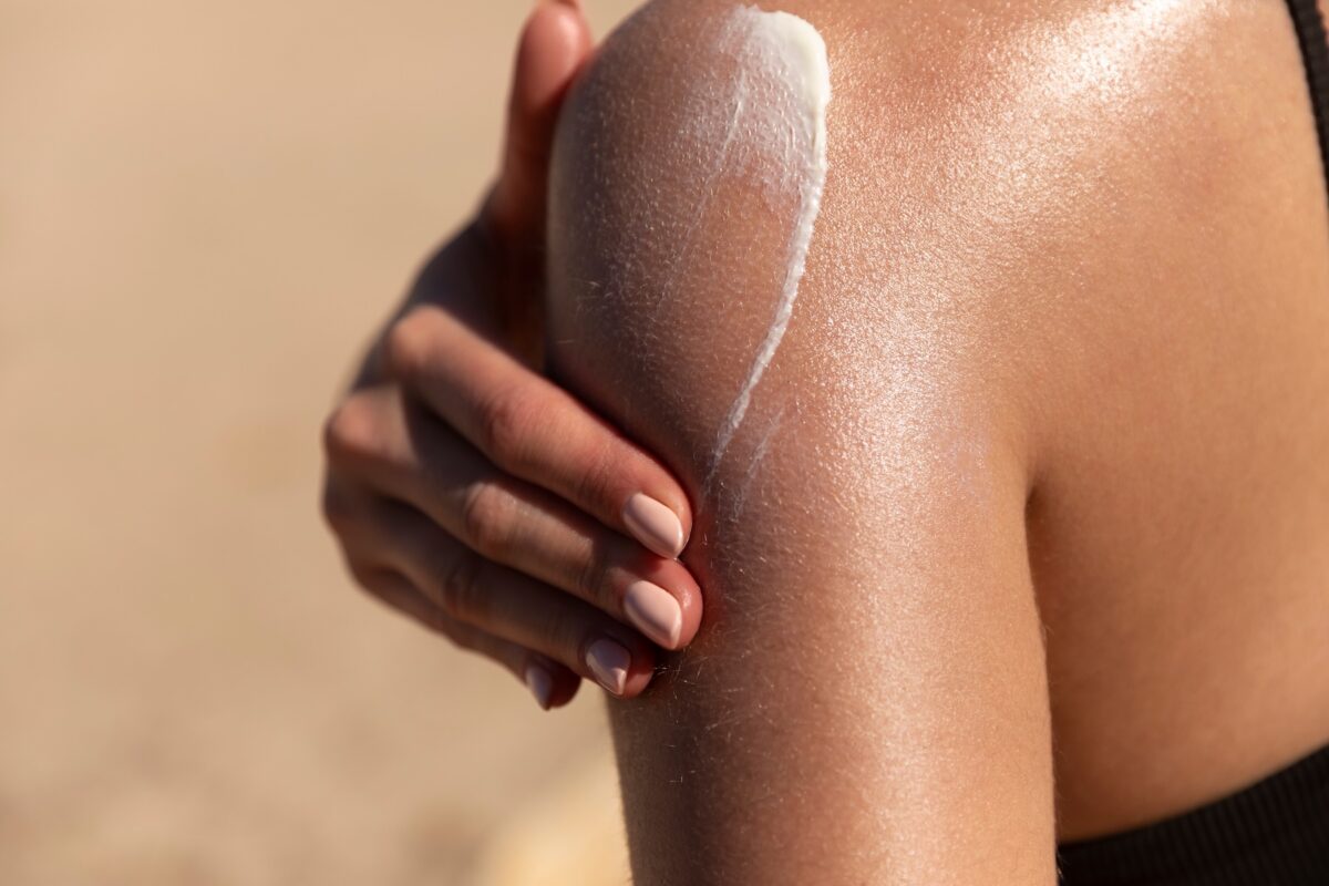 Young woman applying sunscreen on her tanned shoulder