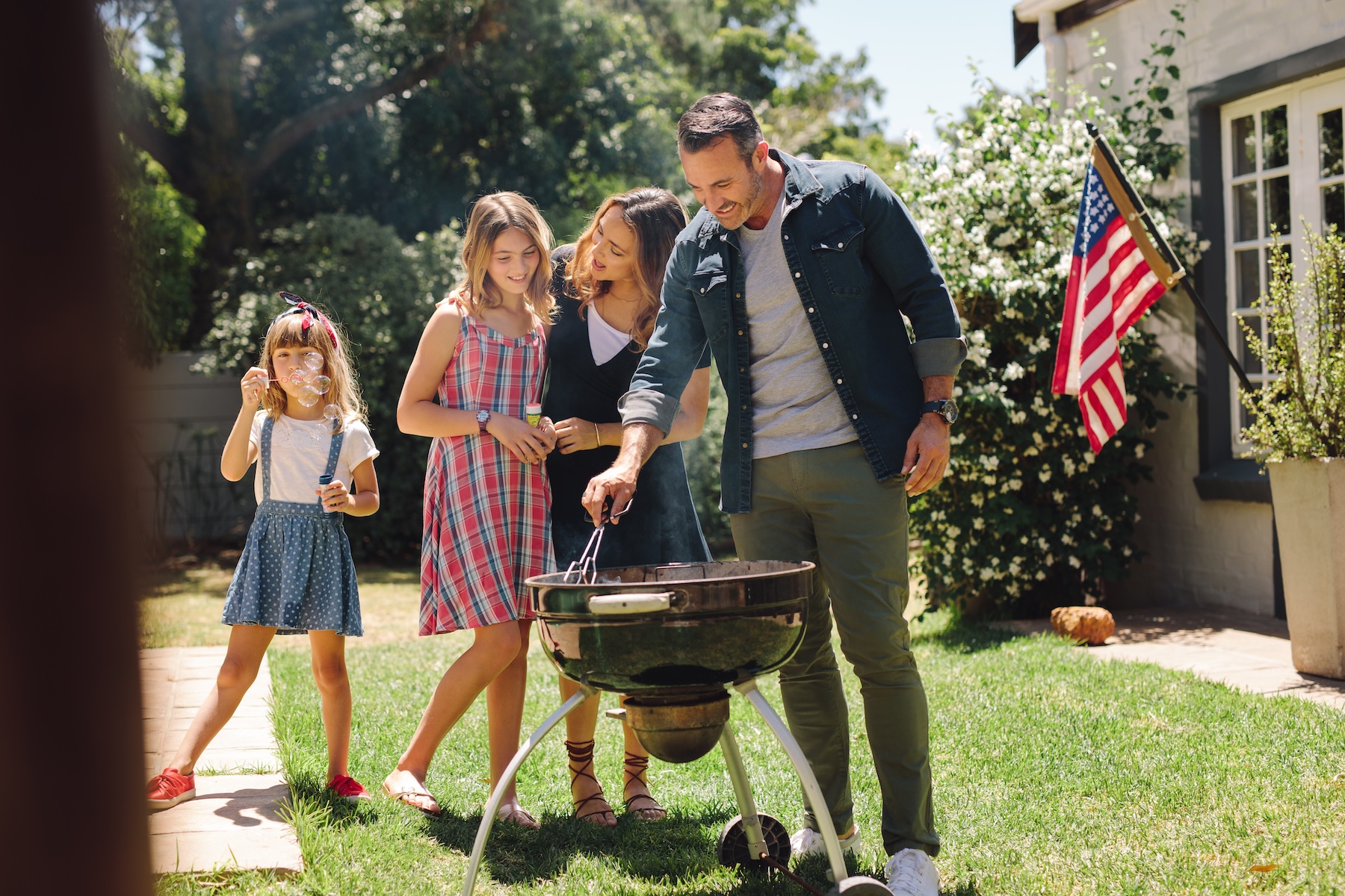 Man grilling barbeque in the backyard standing with his family members.