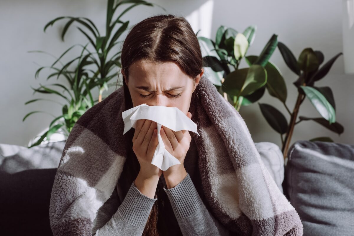 Sick young woman with blanket around her shoulders, blowing her nose