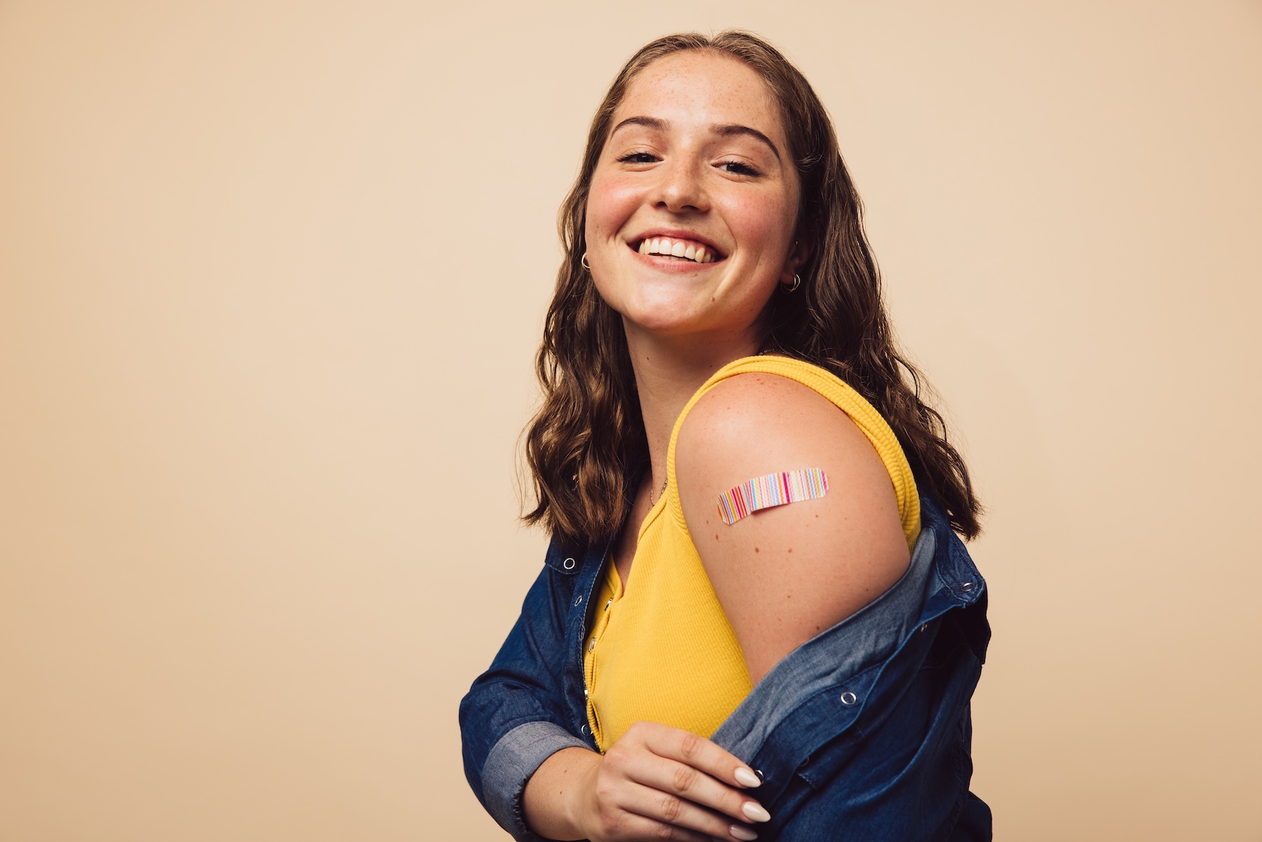 Smiling young woman showing off bandaid on upper shoulder from her flu shot injection.