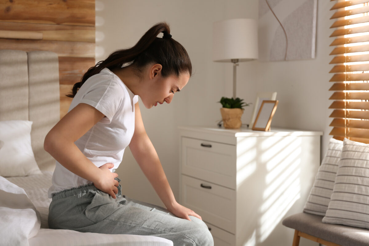A woman is suffering from stomach pain in her room. 