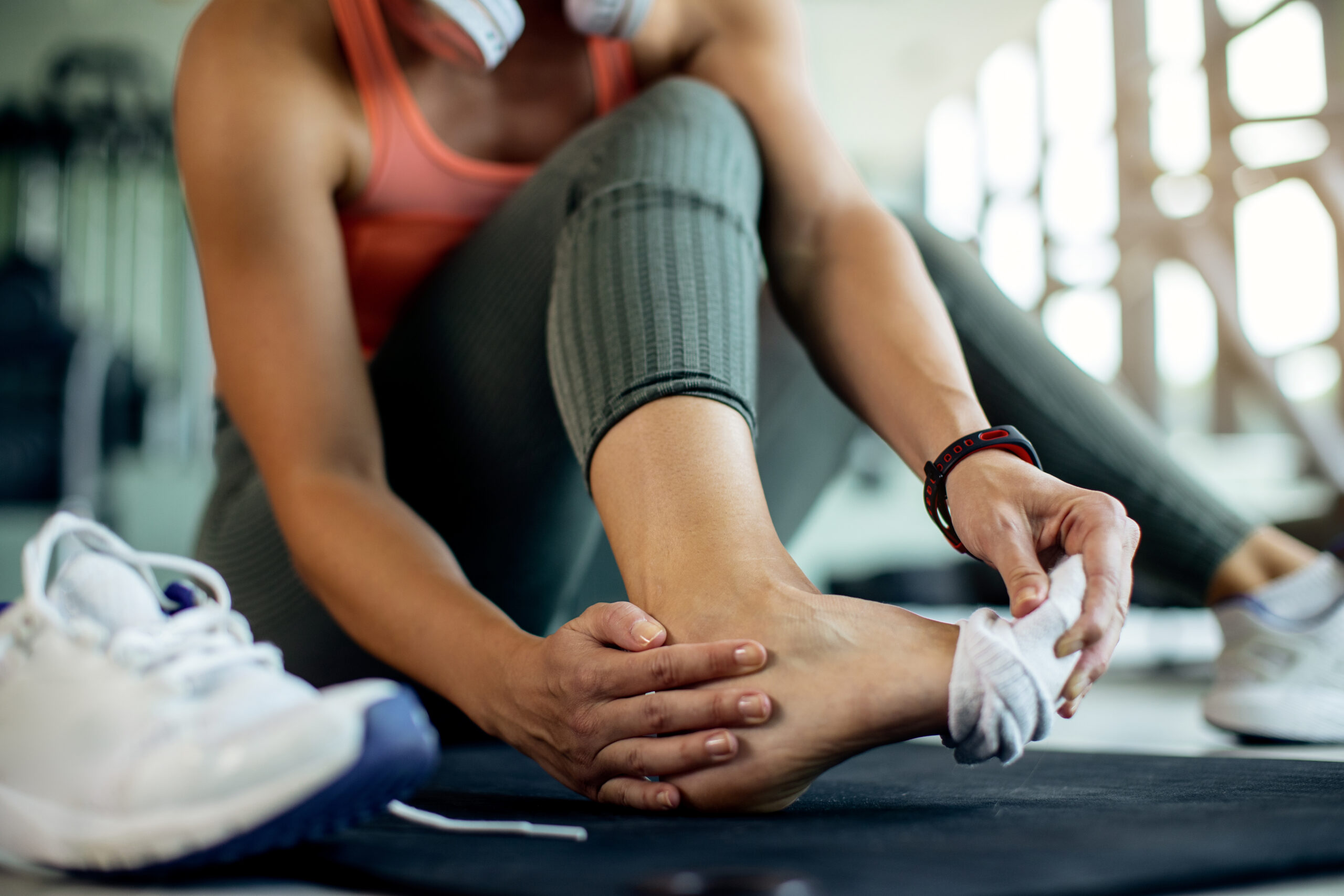 Woman sitting with one of her socks pulled off, touching her ankle.