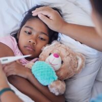 Mother touching sick daughters forehead while checking thermometer