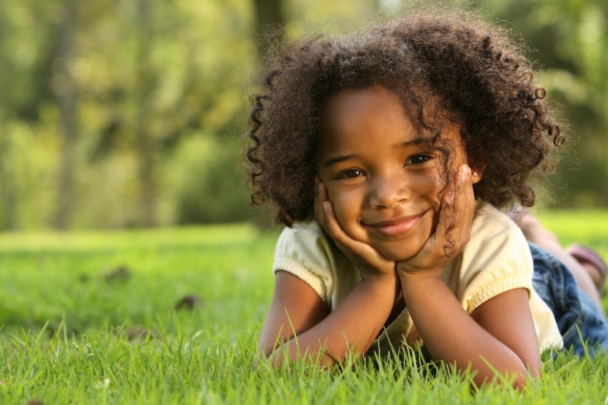 Close up of a smiling African American female toddler lying outside in the grass