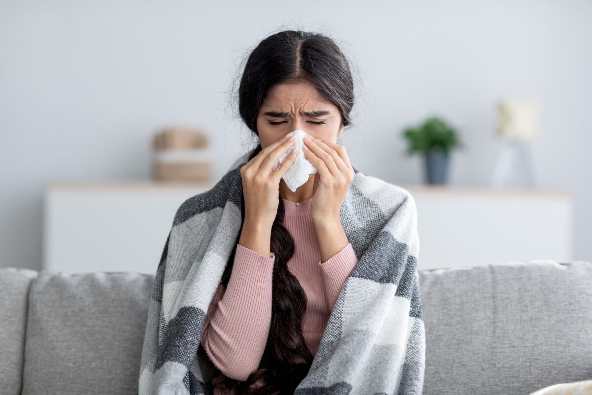 Sick young female wrapped in a plaid blanket suffering from fever and flu on sofa