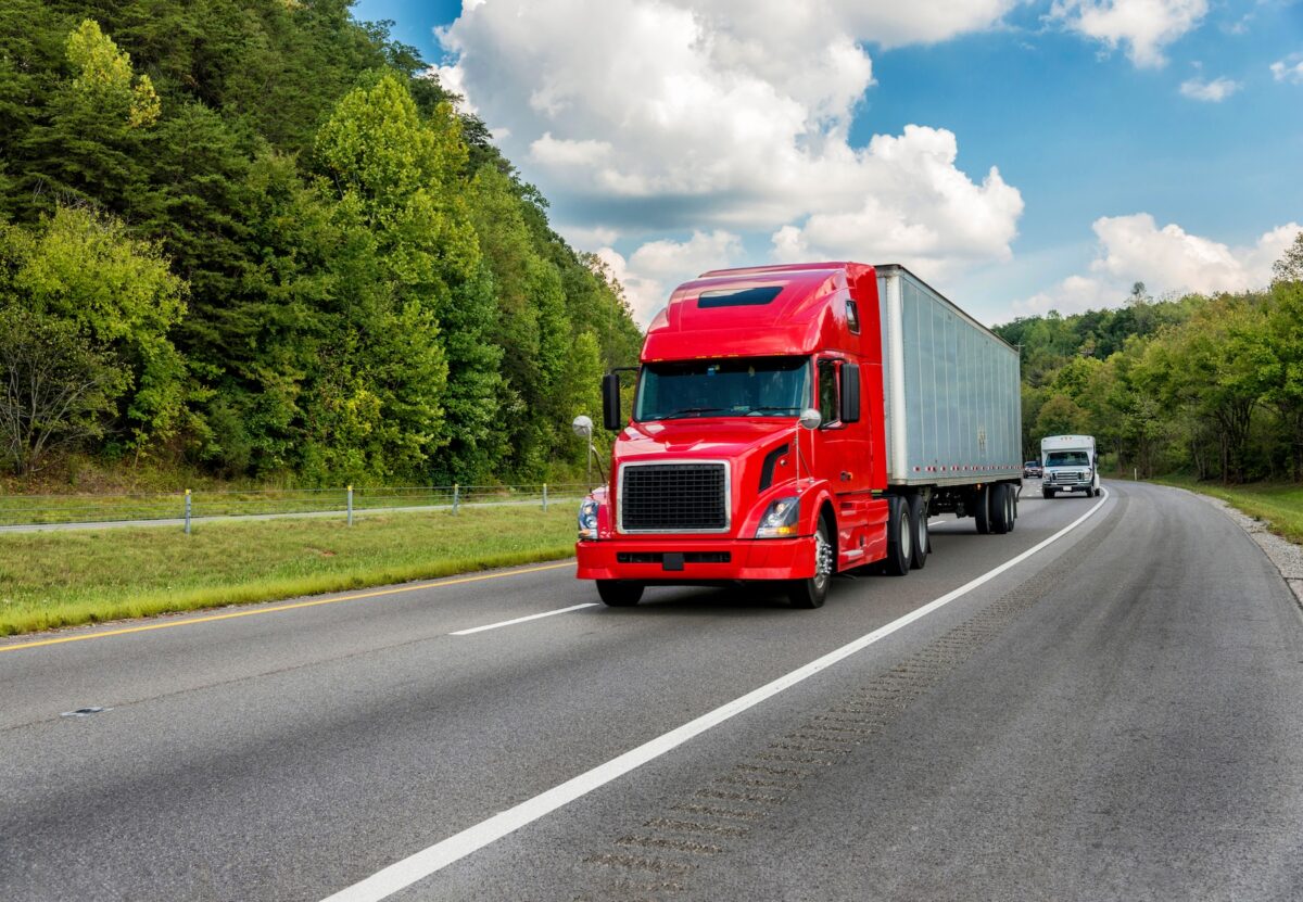 Horizontal shot of a red semi truck going down an interstate highway.