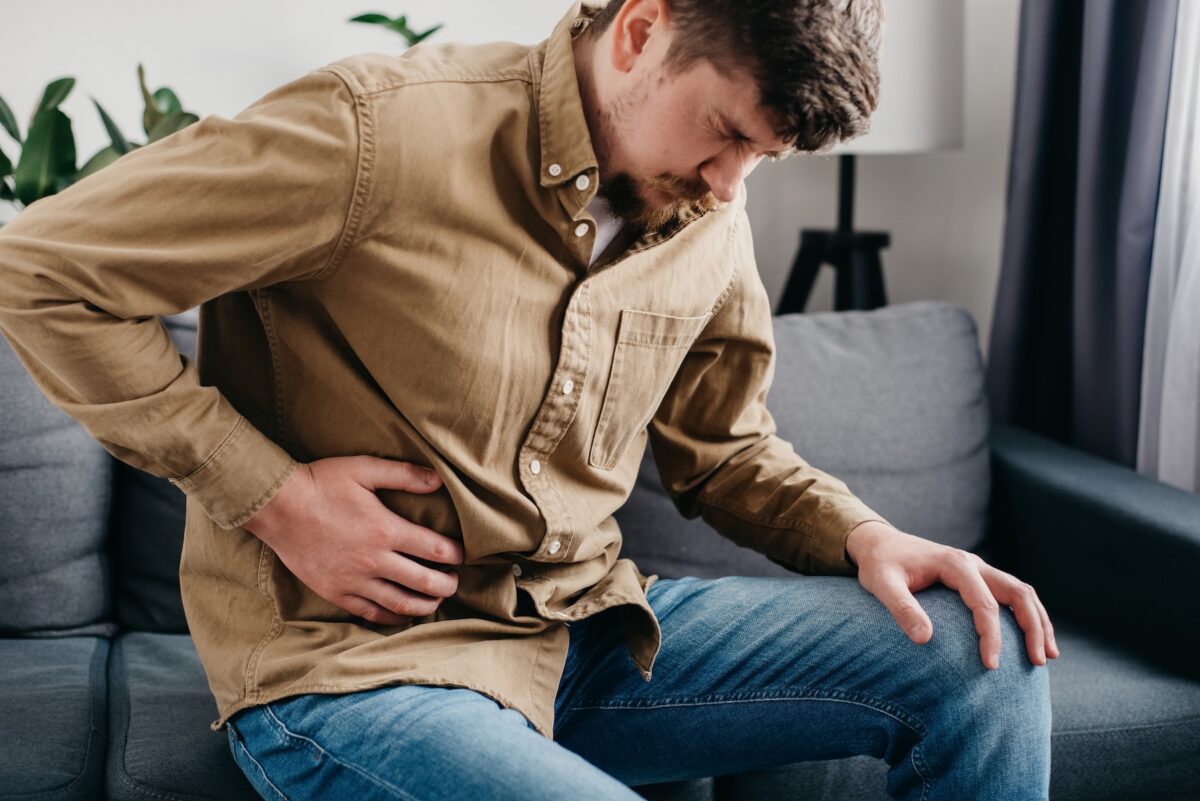 Young man holding belly in pain while sitting on couch